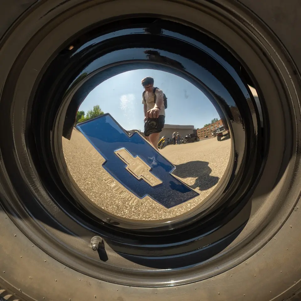 Noah Engle reflected in a chrome hubcap at a car show